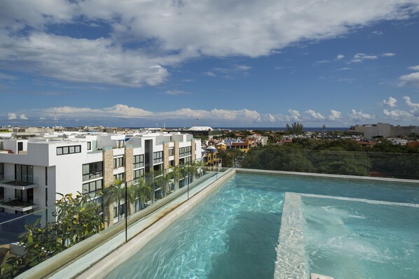A rooftop infinity pool with clear blue water, surrounded by modern buildings and a view of the cityscape.