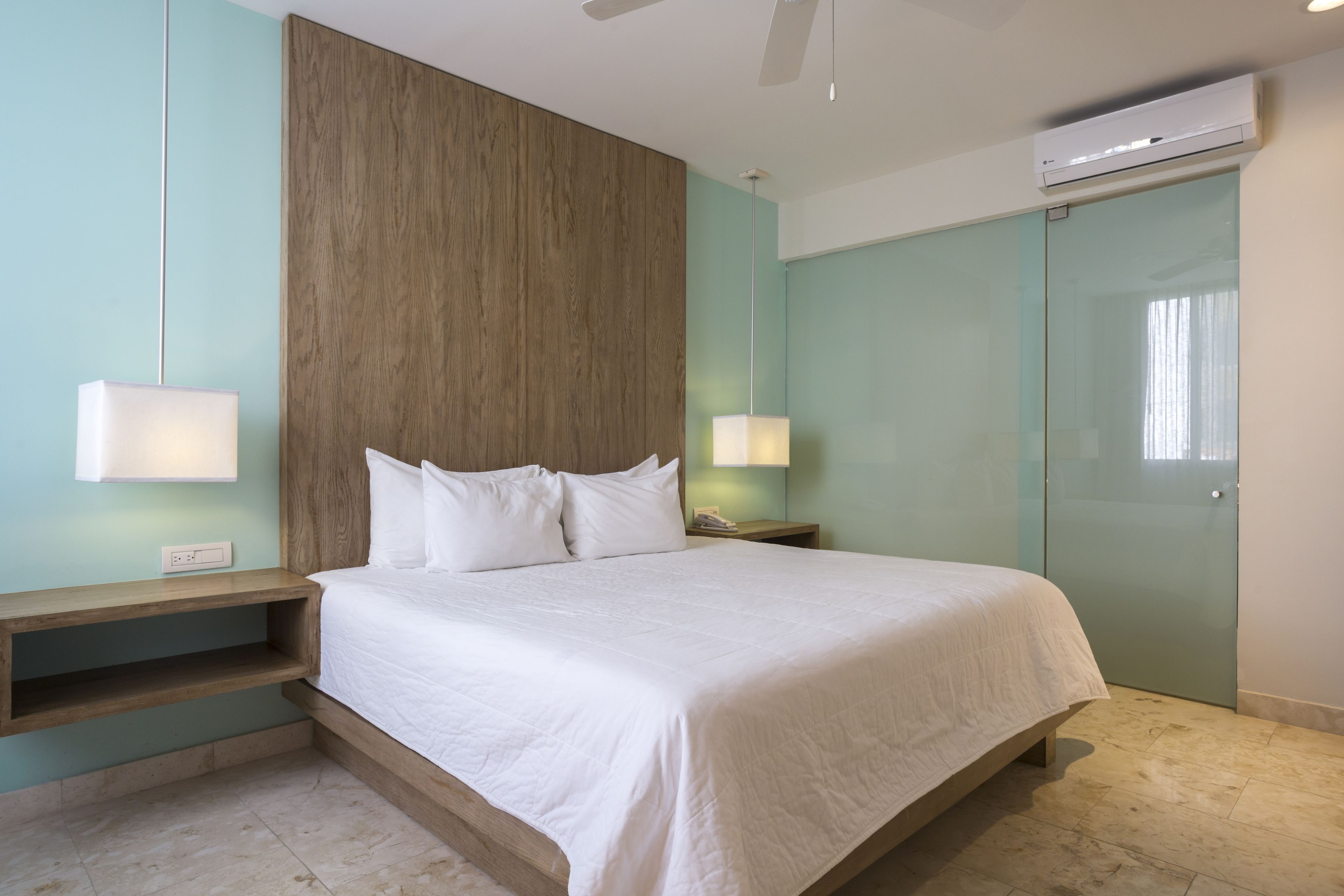 A modern bedroom with a large bed, bedside tables with lamps, a wooden accent wall, and a sliding glass door.