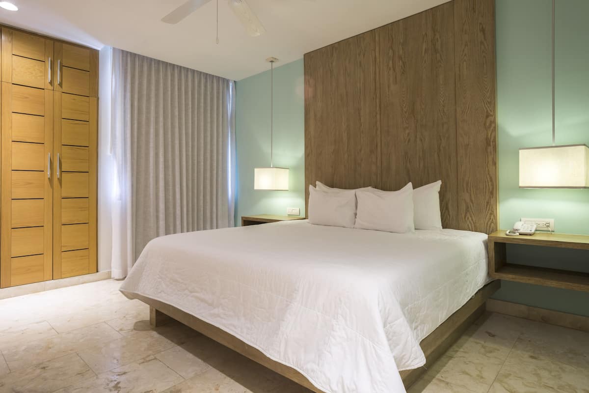 Habitación de hotel con una cama grande, un armario de madera y dos mesitas de noche con lámparas.