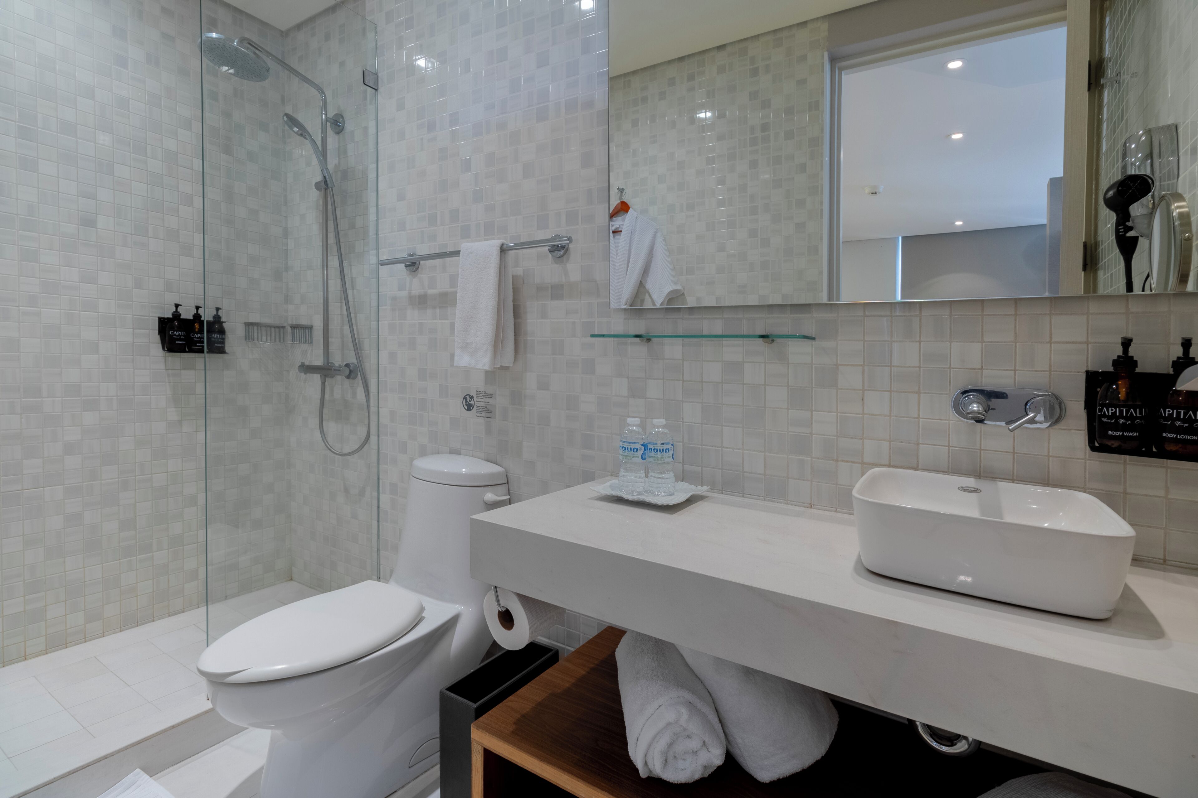 A modern bathroom with a glass-enclosed shower, a white toilet, a sink with a glass shelf, and a mirror above the sink.