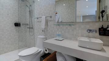 A modern bathroom with a glass-enclosed shower, a white toilet, a sink with a glass shelf, and a mirror above the sink.