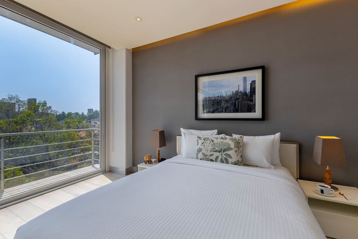 A modern hotel room with a large bed, a cityscape view, and a framed picture on the wall.