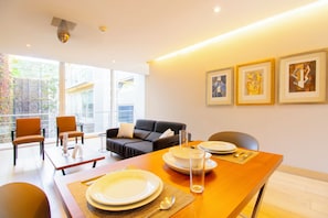 A modern dining area with a wooden table set for four, a sofa, and a balcony with a view.