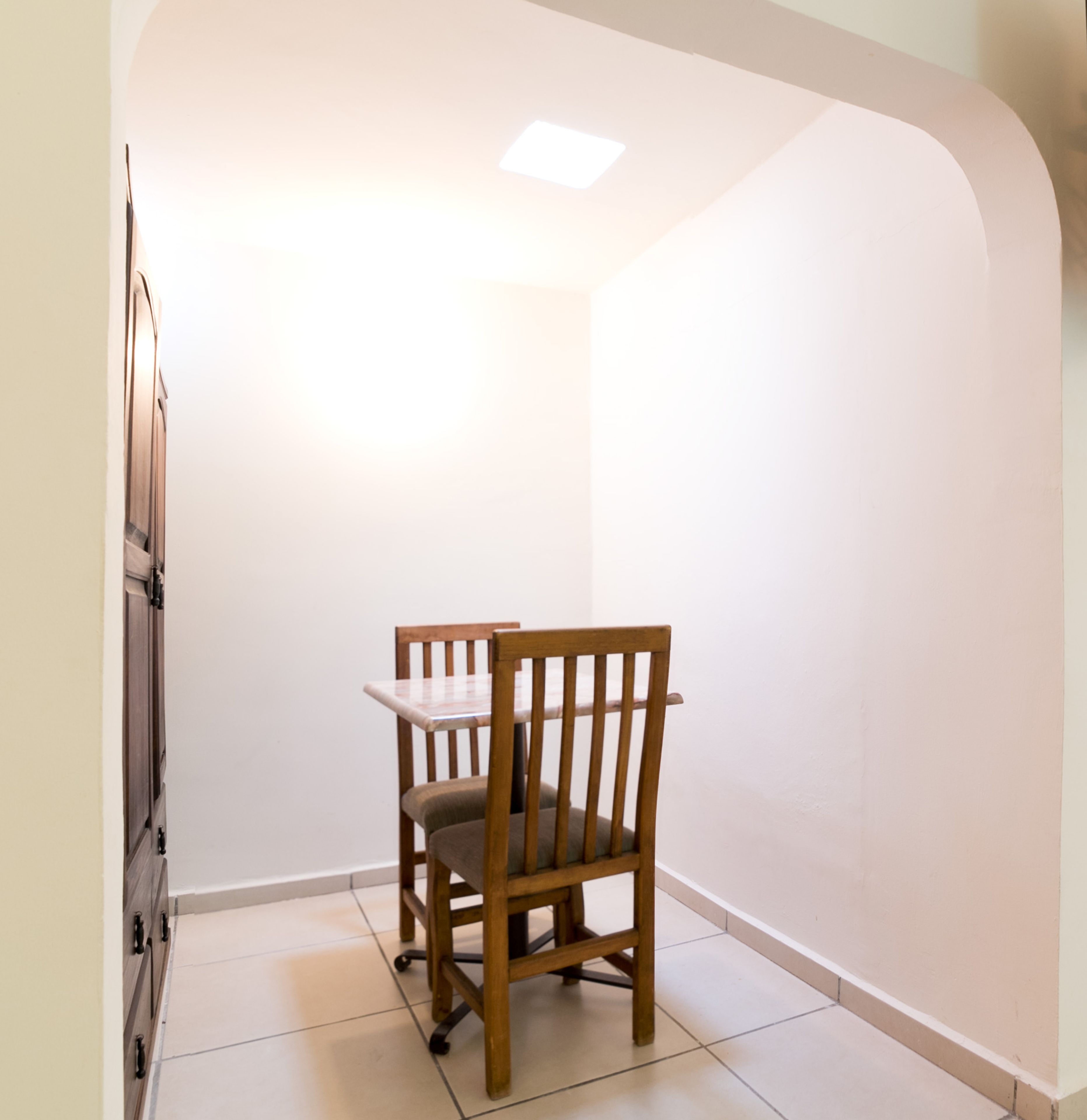 Un pequeño comedor con una silla y mesa de madera, piso de baldosas y pared blanca.