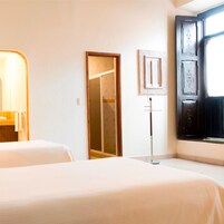 Habitación de hotel con dos camas, una puerta de madera, un ventanal pequeño y una lámpara fijada a la pared.