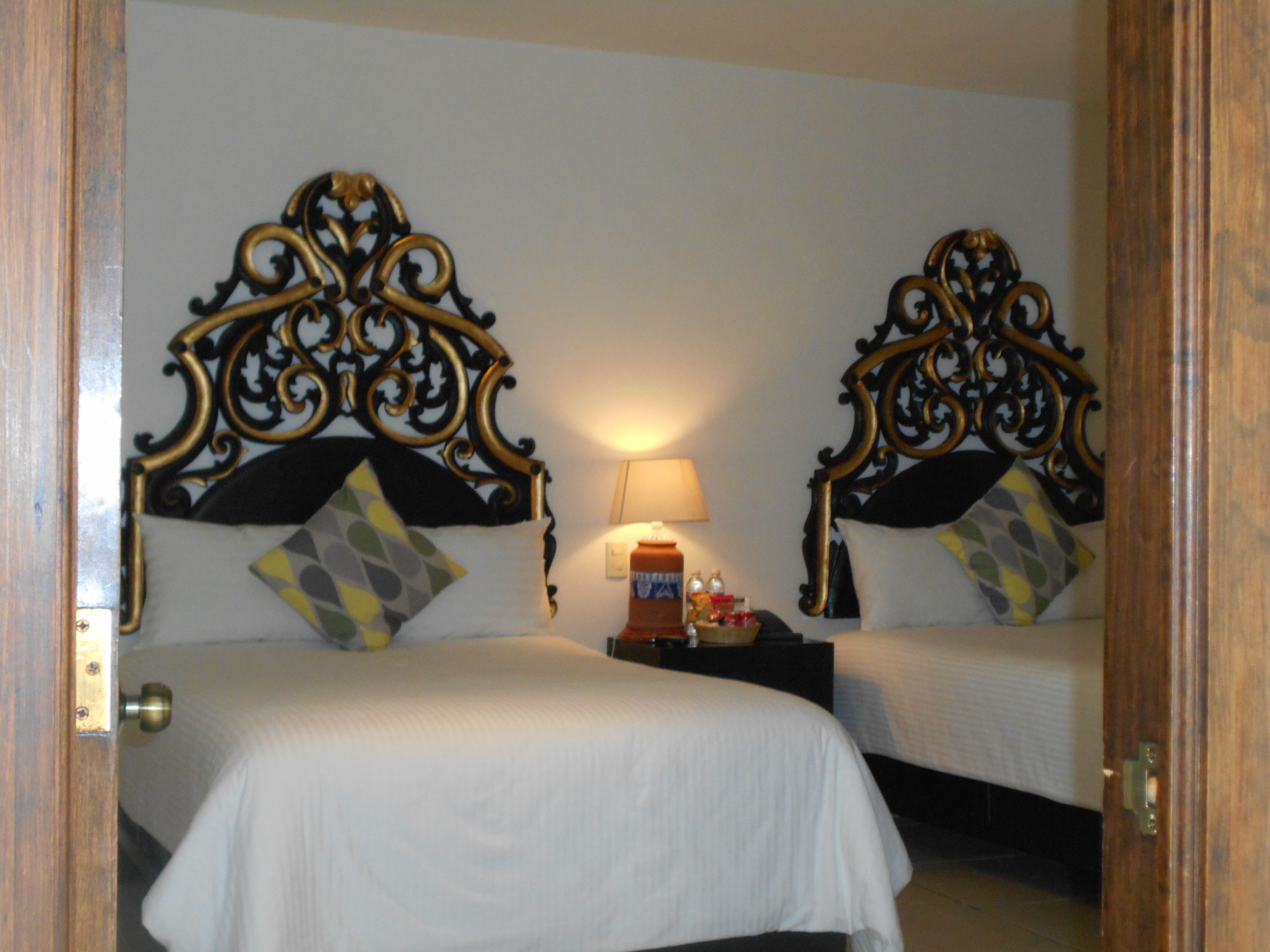 A hotel room with two beds, each with ornate headboards and decorative pillows.