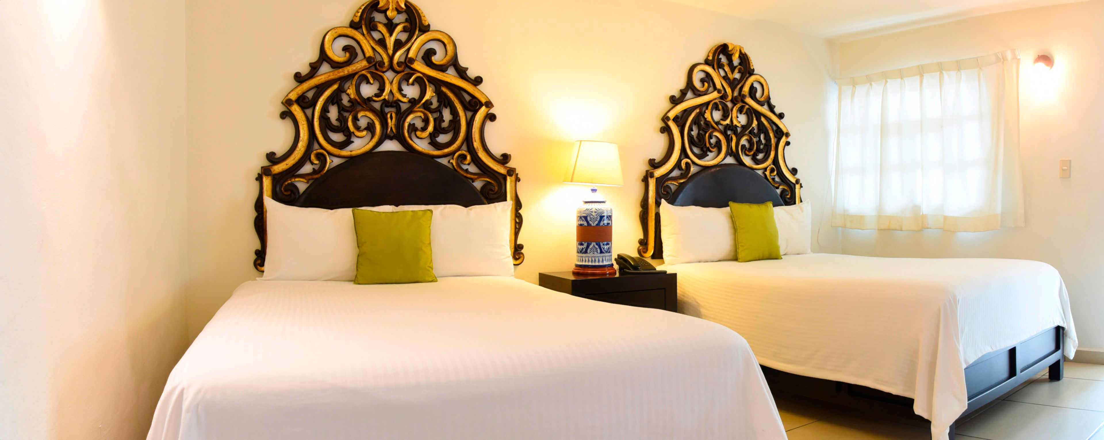 Ein Hotelzimmer mit zwei Betten, jeweils mit aufwendig gestalteten Kopfteilen und einer Nachttischlampe.