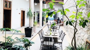Un patio con una mesa de comedor para cuatro personas, rodeado de plantas en macetas y un muro de piedra.
