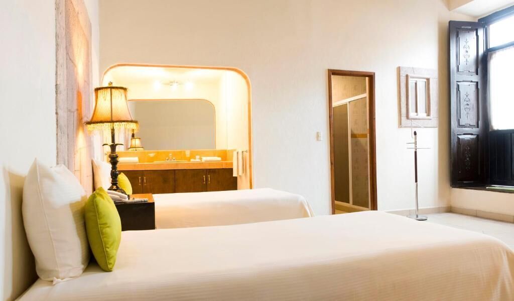 Une chambre d’hôtel avec deux lits, un grand miroir, une coiffeuse avec une lampe et une armoire.