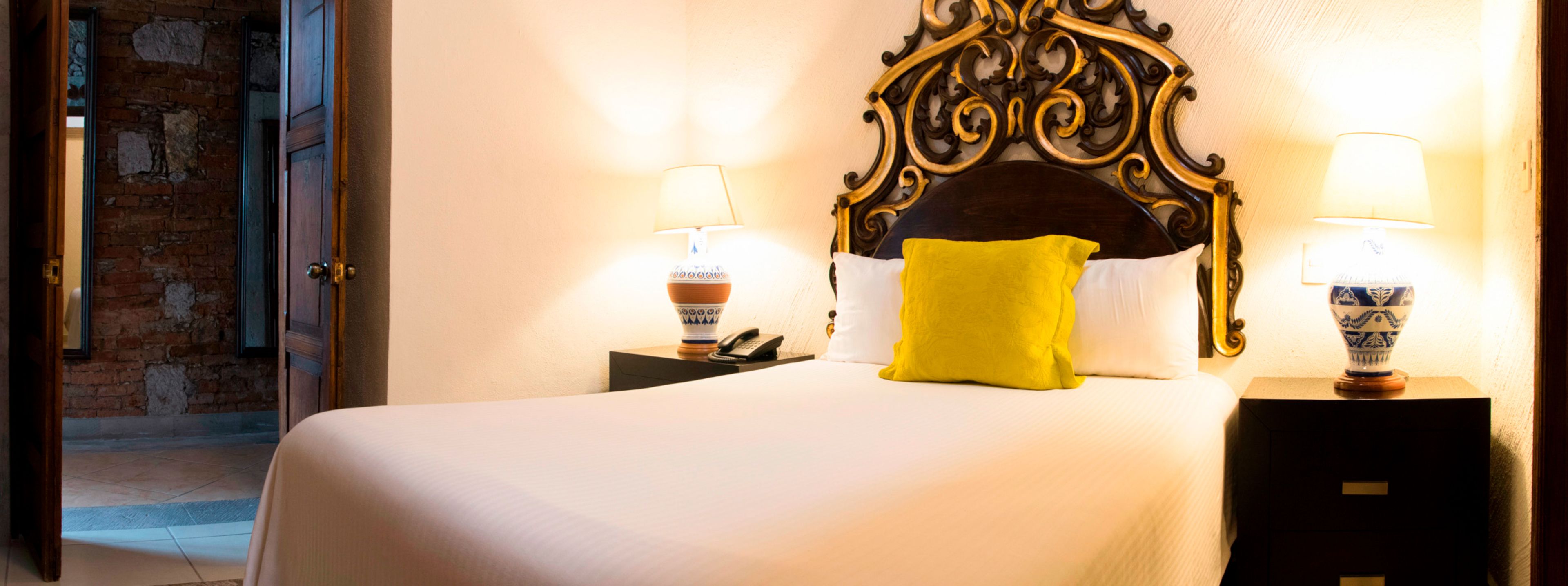 A hotel room with a bed, two bedside lamps, a telephone, and a decorative headboard.