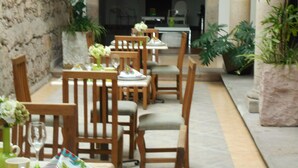 Un comedor con mesas y sillas de madera, un muro de piedra y plantas en macetas.