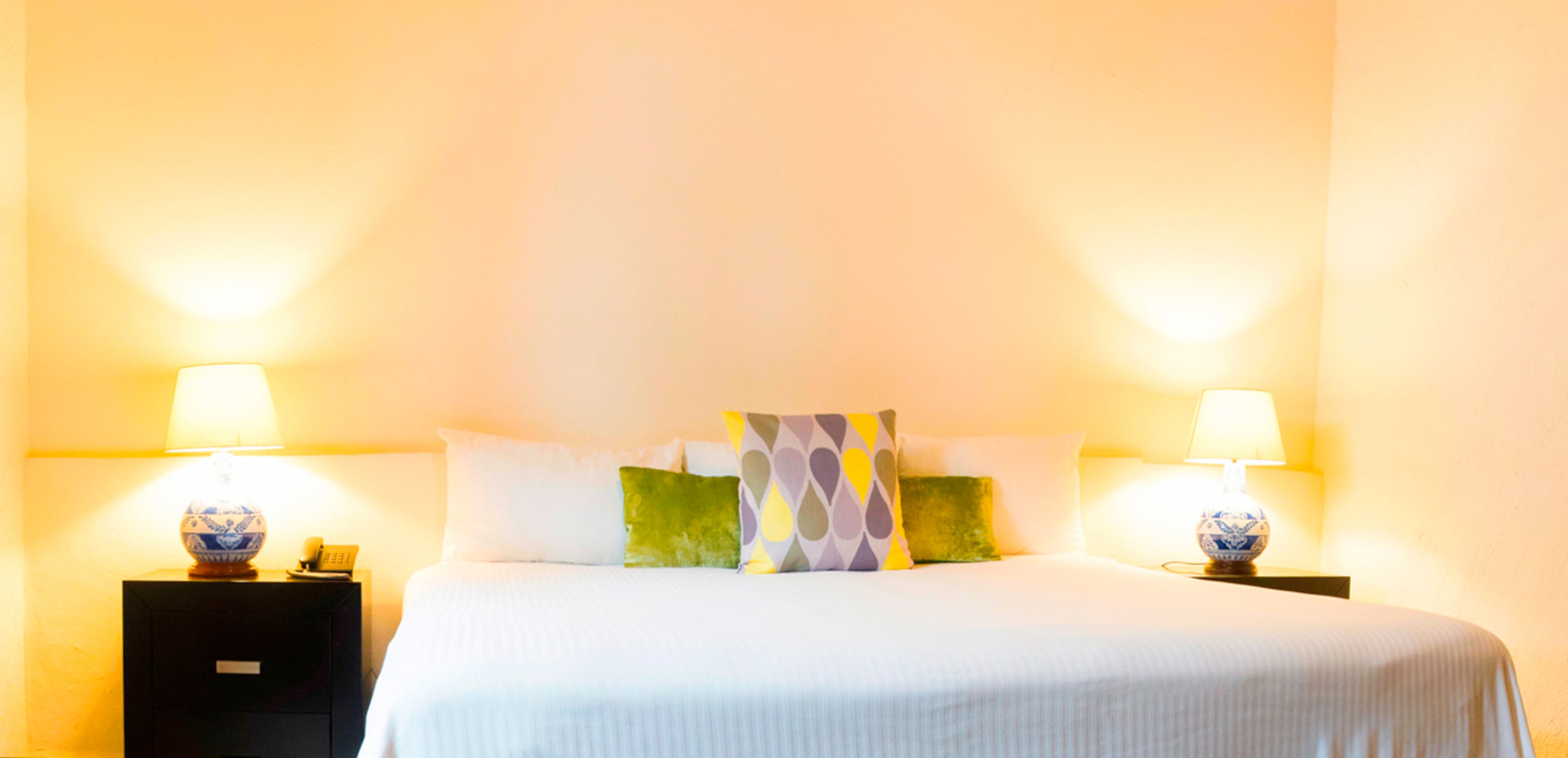 Una habitación de hotel con una cama bien hecha, dos lámparas de noche y una mesita de noche con un teléfono.