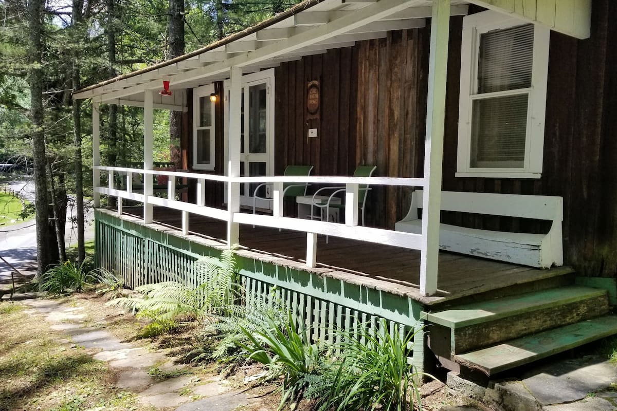A rustic cabin with a porch, a small deck, and a stone pathway leading to the entrance.