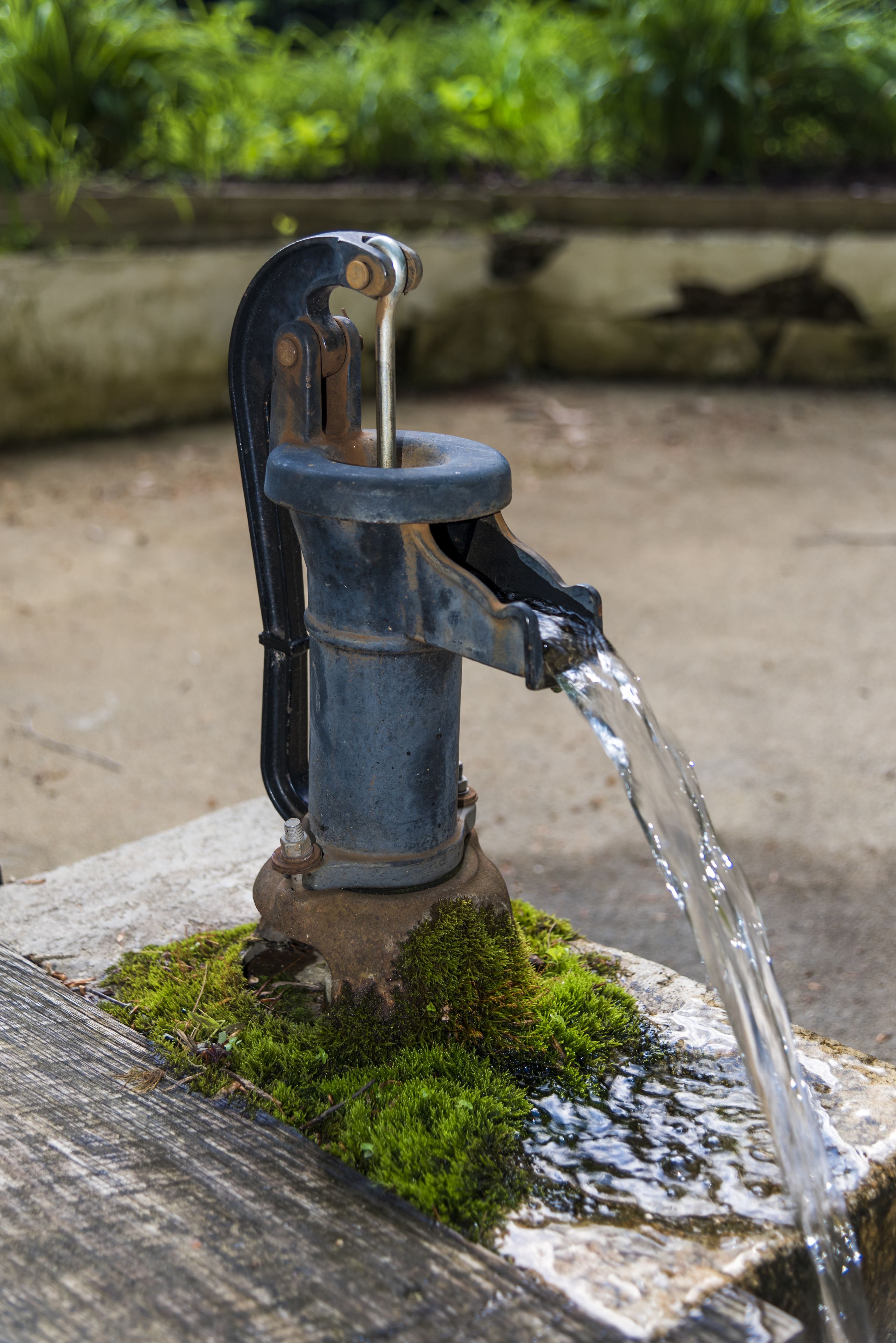 A metal water spout with water flowing from it, placed on a moss-covered stone.