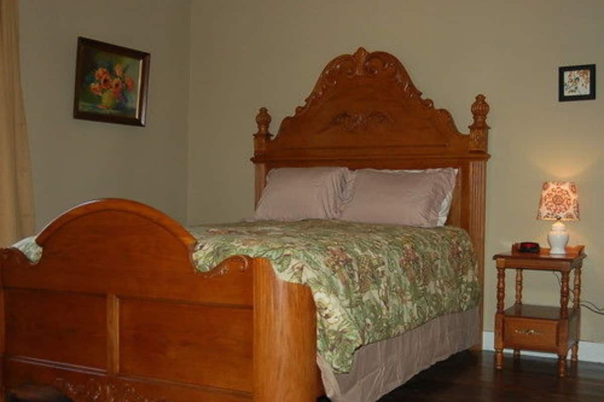A wooden bed with a floral bedspread, a bedside table with a lamp, and a framed painting on the wall.