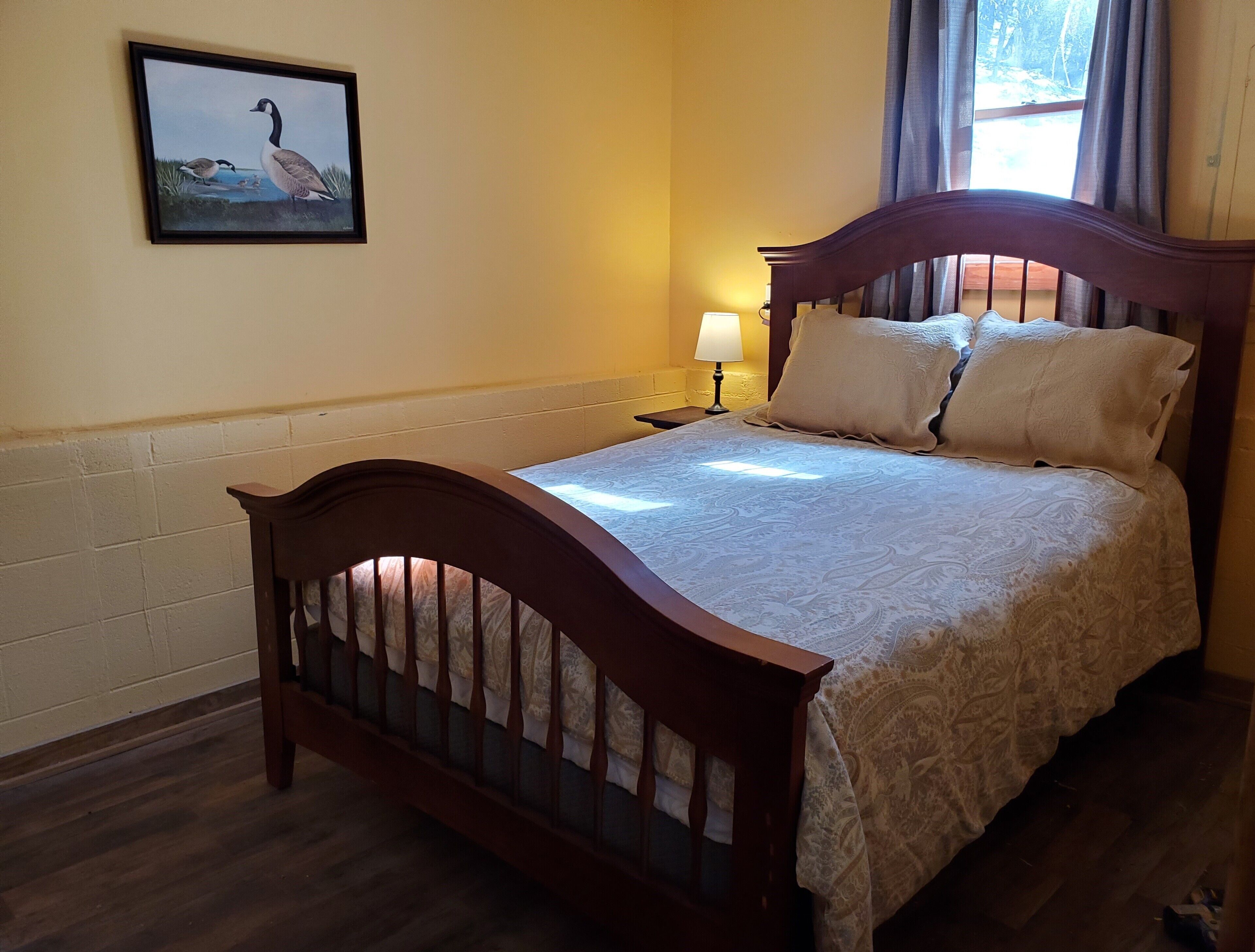Un dormitorio con una cama de madera, una mesita de noche, una lámpara y un cuadro en la pared.