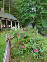 Uma casa rústica de madeira com varanda e jardim cheio de flores cor-de-rosa.