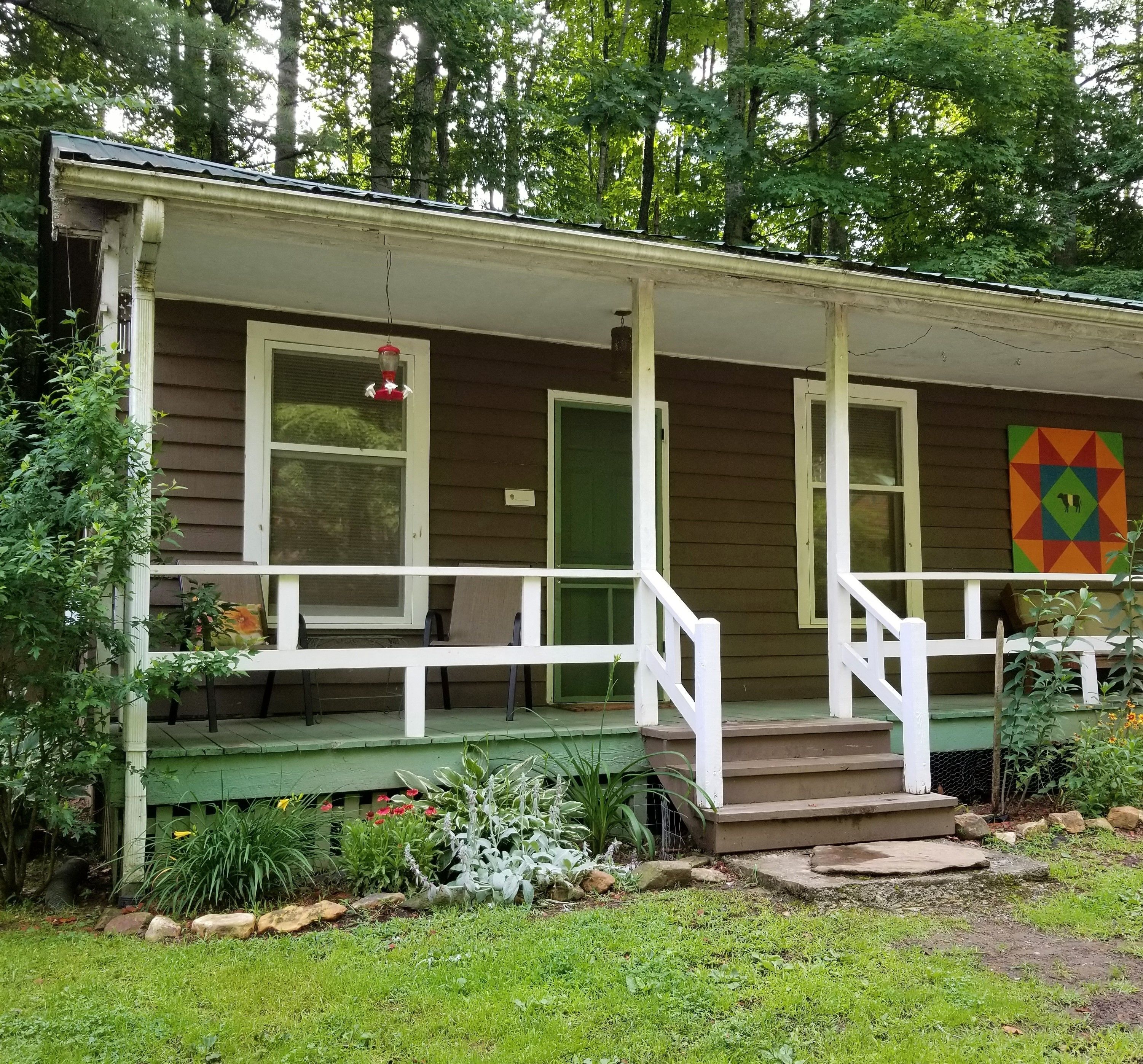 A wooden house with a porch, a red bird feeder, and a colorful quilt on the wall.