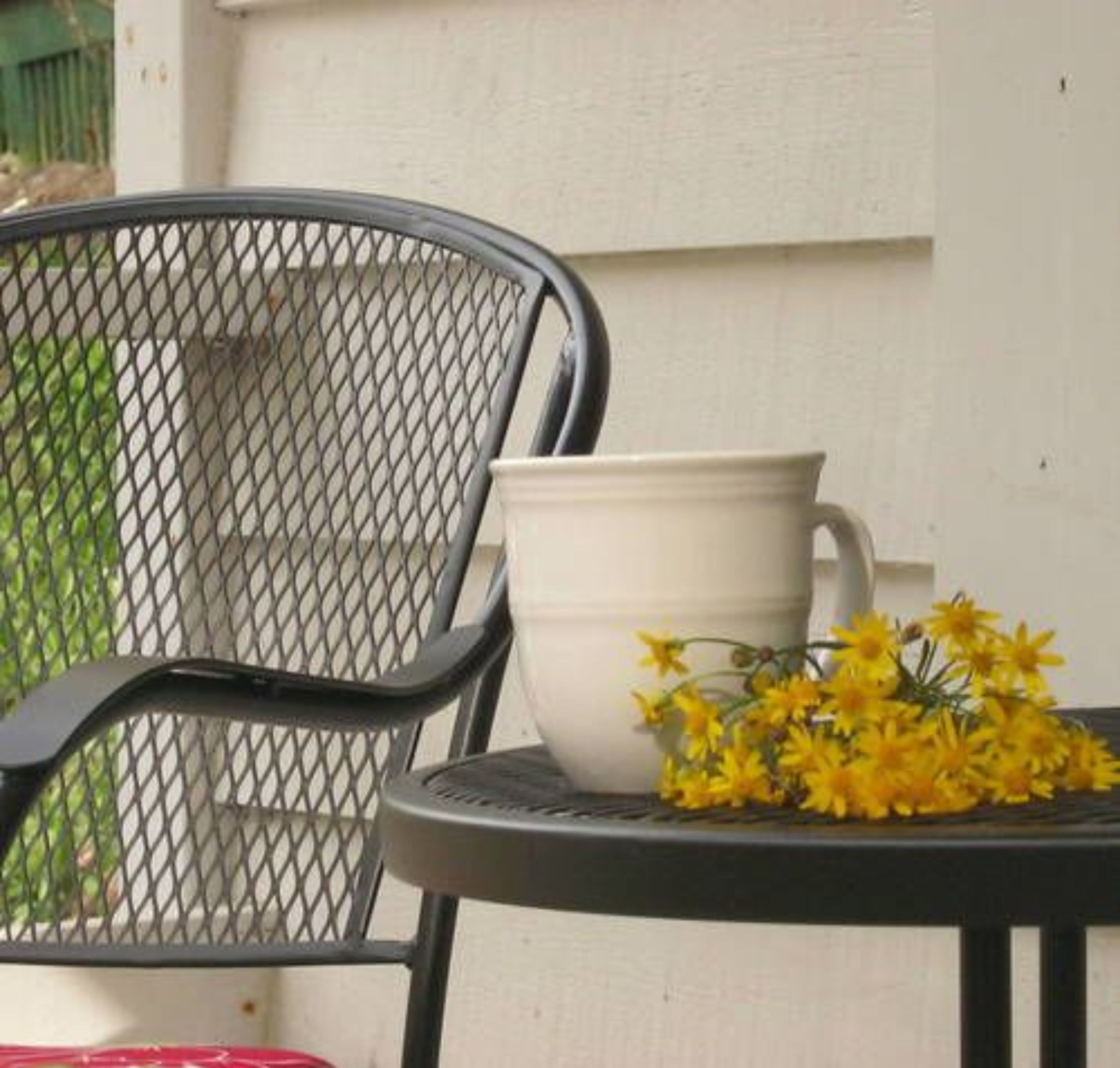 A metal chair and a white pot with yellow flowers on a table.