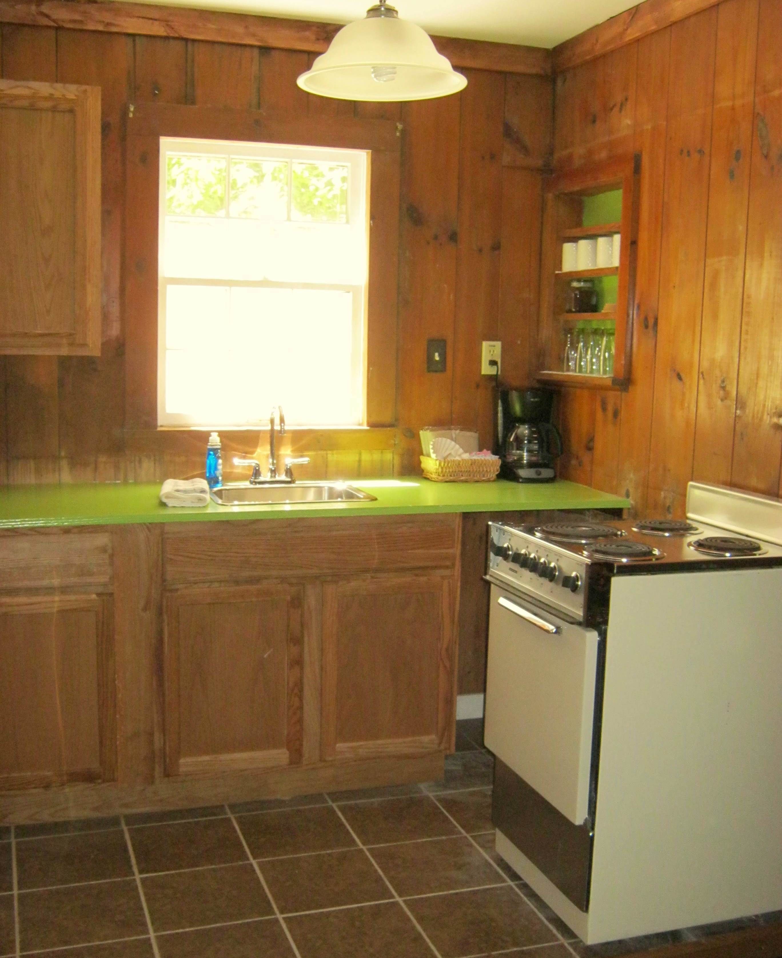 A kitchen with wooden cabinets, a green countertop, a sink, a stove, and a window.