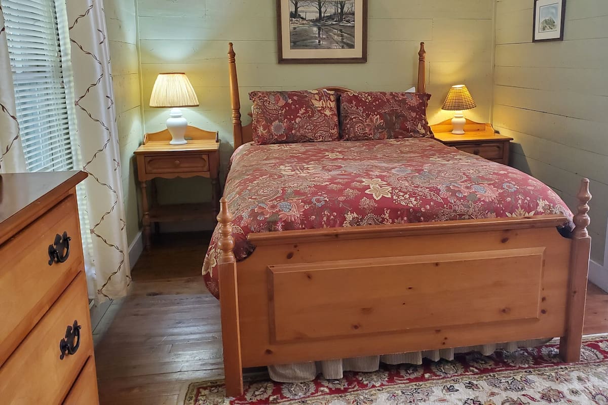 A wooden bed with a floral bedspread, two bedside lamps, a nightstand, a wooden dresser, and a patterned rug.