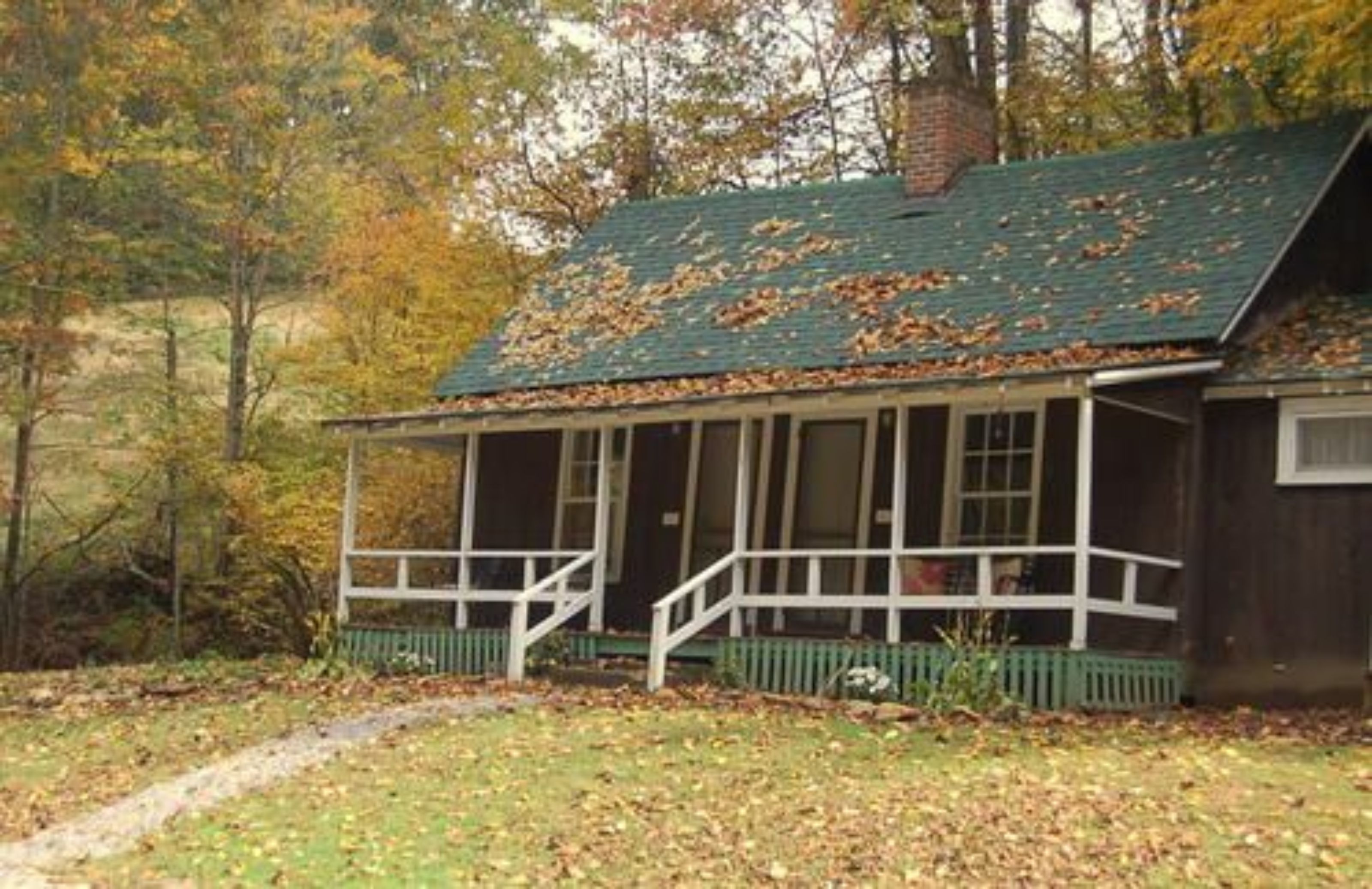 Una baita rustica con un portico, circondata da alberi e foglie cadute.