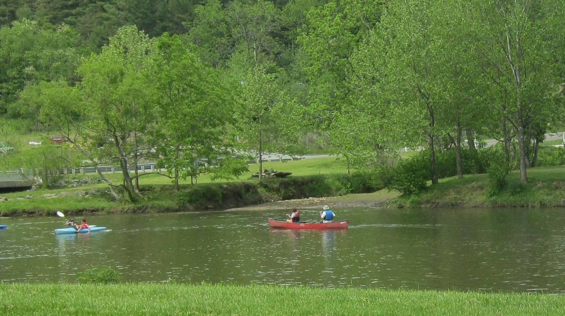 A calm river with kayaks and a canoe, surrounded by lush greenery and trees.