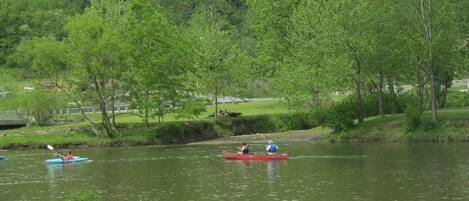 A calm river with kayaks and a canoe, surrounded by lush greenery and trees.