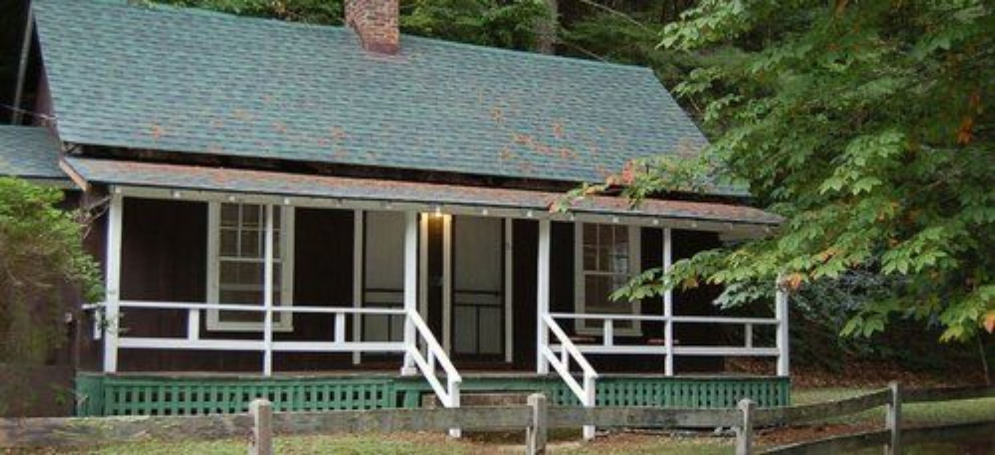 A two-story cabin with a porch, surrounded by trees.