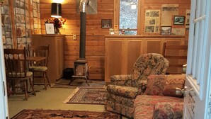 Acogedor interior de cabaña con paredes de madera, chimenea, un sillón estampado y una alfombra grande.