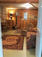 Interior acolhedor de uma cabana, com detalhes em madeira, lareira, poltrona estampada e um tapete grande.