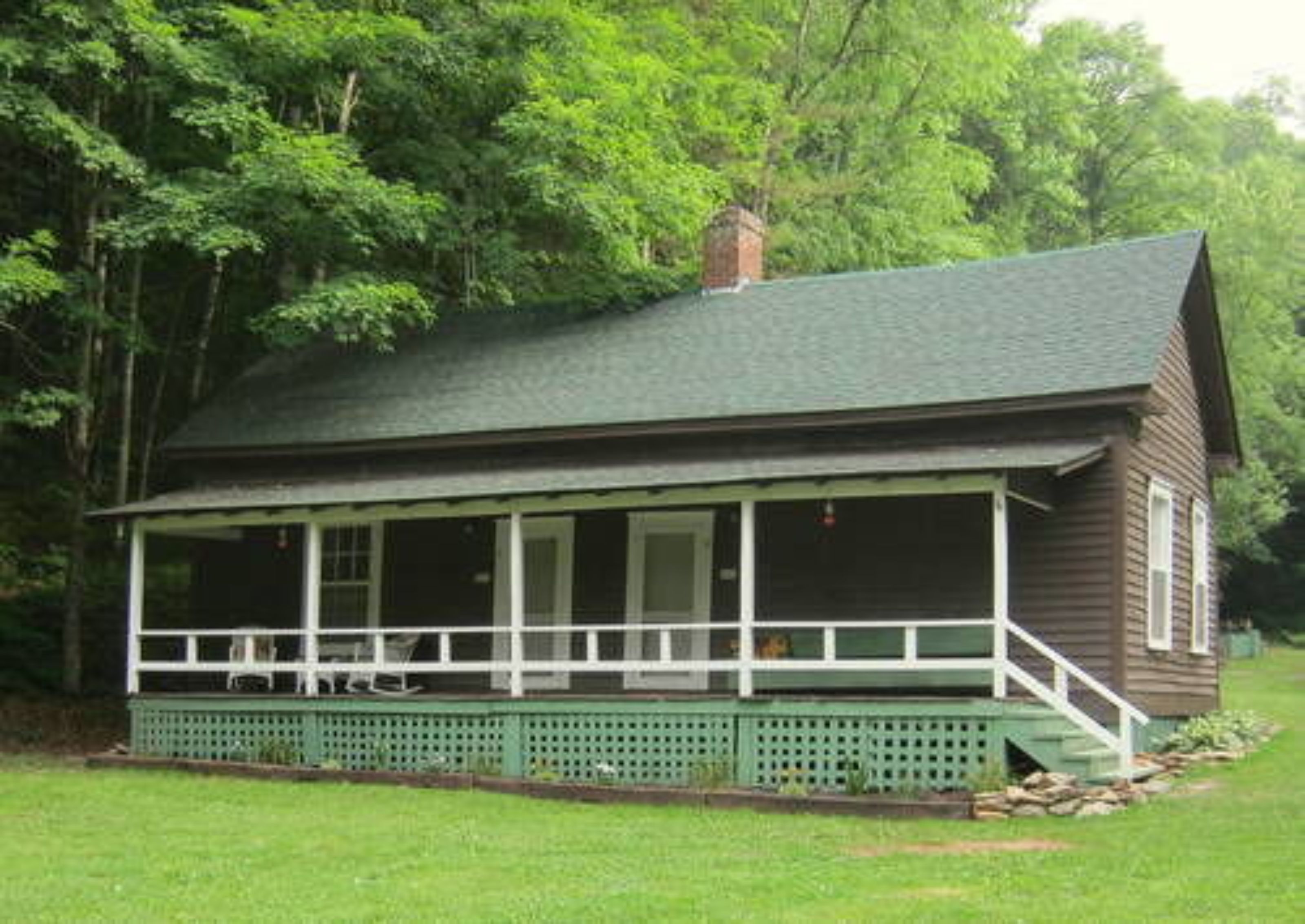A wooden cabin with a porch, surrounded by trees.