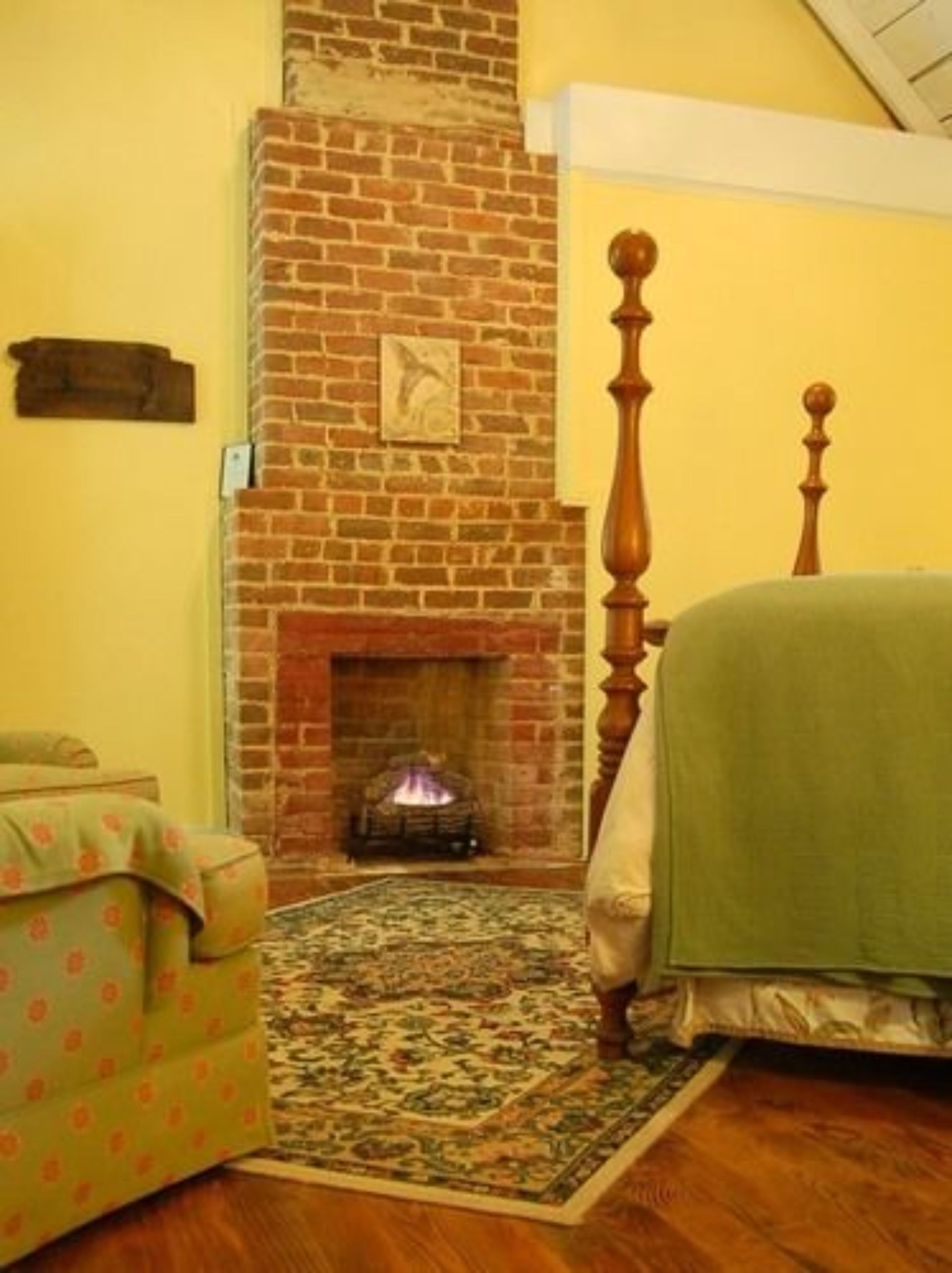 Une pièce avec une cheminée en briques, un lit en bois, une couvre-lit verte et un tapis à motifs.