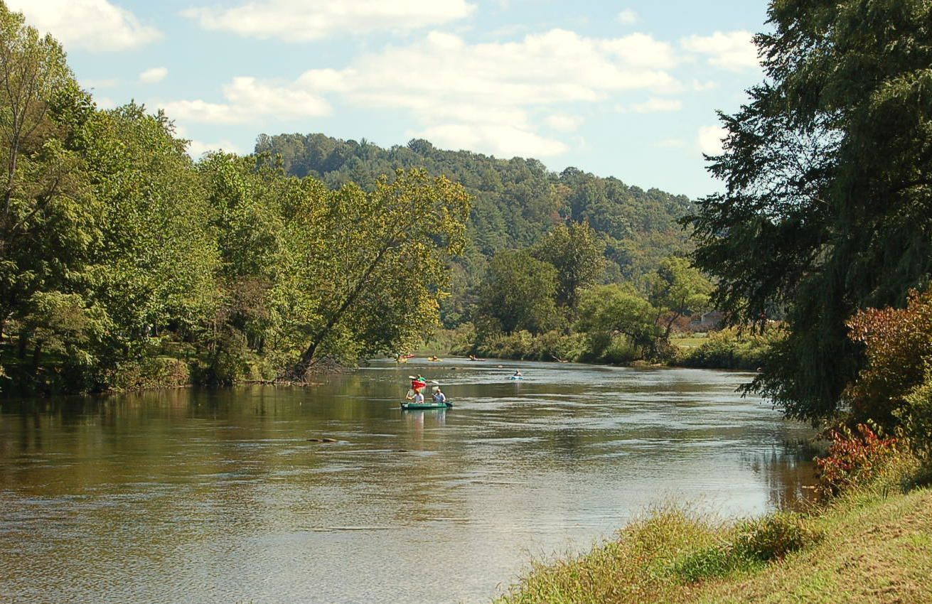 Une rivière paisible, où l’on peut naviguer, bordée d’une forêt dense et entourée de collines.