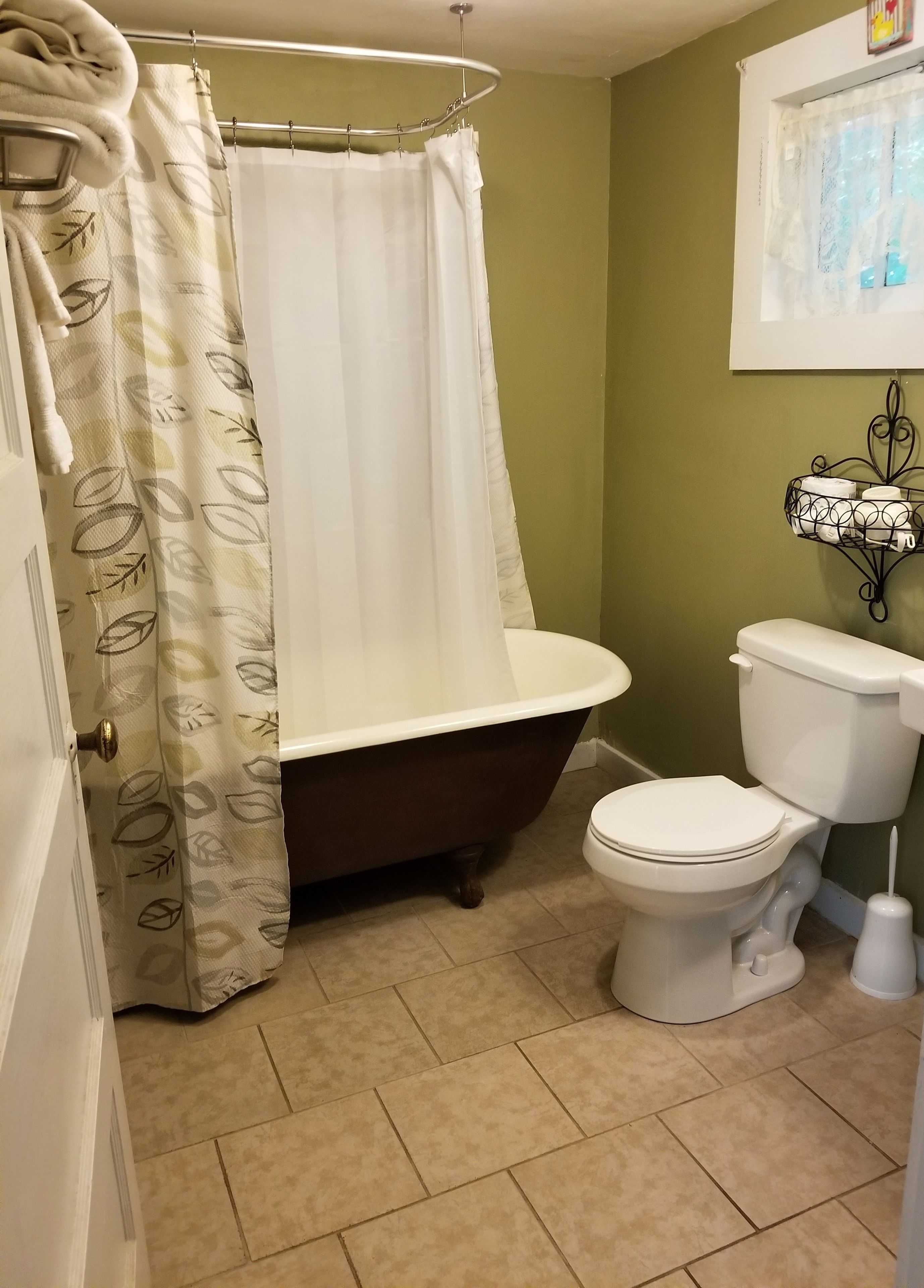 Un baño con bañera, inodoro y cortina de ducha con estampado de hojas.