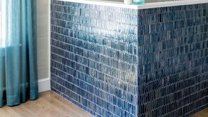 Un espace d’accueil avec un mur recouvert de carreaux bleus, un comptoir d’accueil en bois et un luminaire suspendu.