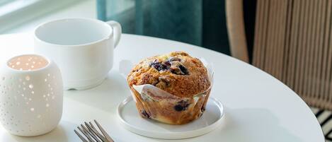 A table with a muffin, a white mug, and a fork.