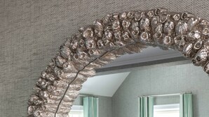 Une pièce avec un grand miroir décoratif, un canapé bleu, une chaise en bois et une petite table sur laquelle est posée une plante.
