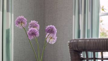 A room with a wicker chair, a blue sofa, a patterned pillow, a vase with purple flowers, and a textured wall.