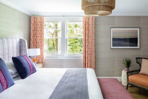 A hotel room with a large bed, a chair, a window with curtains, a wall-mounted picture, and a hanging light fixture. - The Sydney, The Edgartown Collection (Edgartown)