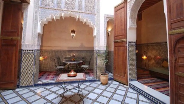 A traditional Moroccan interior with a tiled courtyard, a dining area with a table and chairs, and ornate wooden doors and arches. - Riad Dar Benares (Fes)