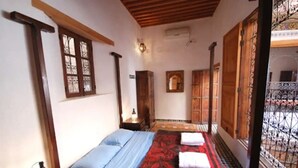A room with a bed, a nightstand, a wall-mounted lamp, and a window with a metal gate. - Riad Dar Benares (Fes)