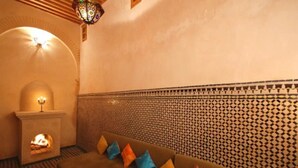 A cozy room with a fireplace, patterned wall, and a sofa with colorful cushions. - Riad Dar Benares (Fes)
