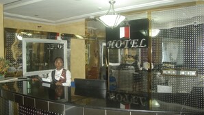 A hotel reception desk with a receptionist, a large mirror, and a sign that reads "HOTEL." - DK Hotel (Bonaberi)