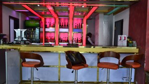 A bar area with a counter, shelves of bottles, and three stools. - DK Hotel (Bonaberi)