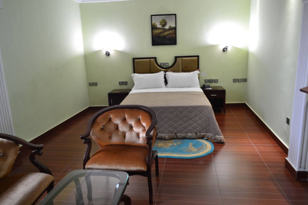 A bedroom with a bed, two bedside tables, a chair, a small table, and a rug.