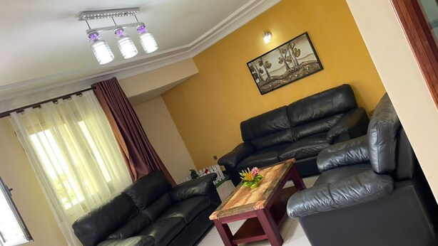 A living room with a black leather sofa set, a wooden coffee table, and a ceiling light fixture. - DK Hotel (Bonaberi)
