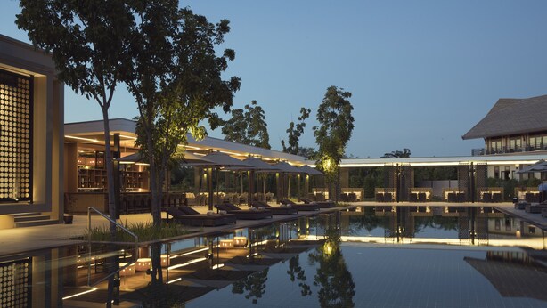 A serene pool area with lounge chairs and umbrellas, surrounded by modern buildings and trees. - Emerald Palace Hotel (Naypyidaw)