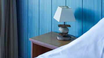 En snyggt bäddad säng med vita sängkläder, en sänglampa med en vit lampskärm och ett träbord bredvid sängen med en hög stenar på.