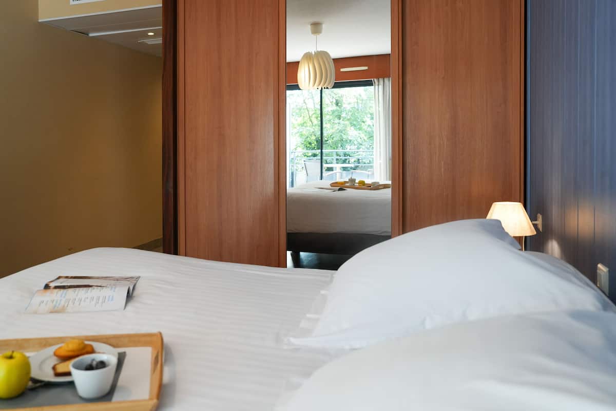 A hotel room with a bed, a tray with breakfast items, a window with a view, and a lamp.